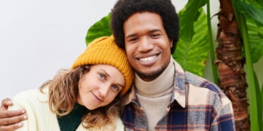 A woman sitting next to a man. She leans her head on his shoulder, he is laying his hand around hers.