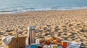 A blanket with snacks and drinks at the beach for a picnic.