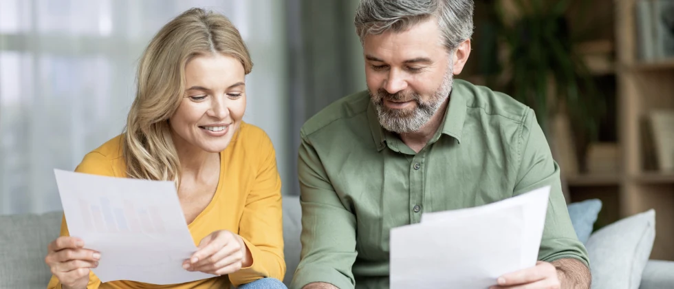 A couple holding papers and sitting on the couch chatting.