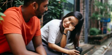 A woman and a man sitting, chatting and smiling at each other, showing how to get a guy to ask you out