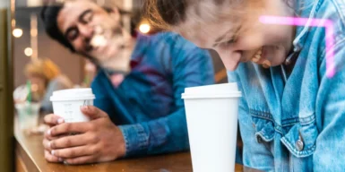 A man and a woman drinking coffee and laughing together showing how to ask out a stranger.