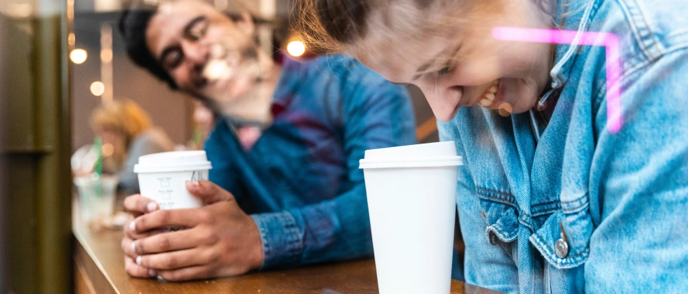 A man and a woman drinking coffee and laughing together showing how to ask out a stranger.