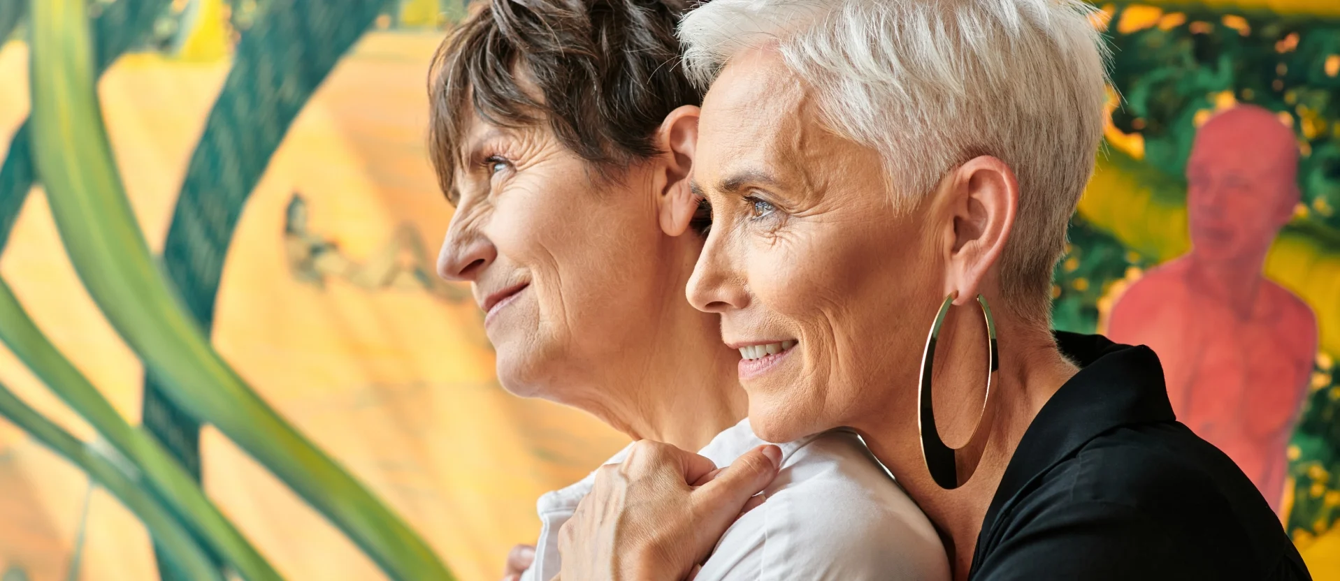 Mature lesbian couple embracing and smiling warmly.